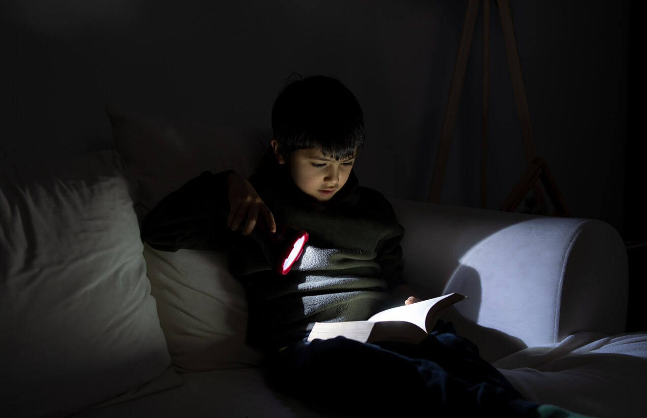 child holding a flashlight on a book in the dark