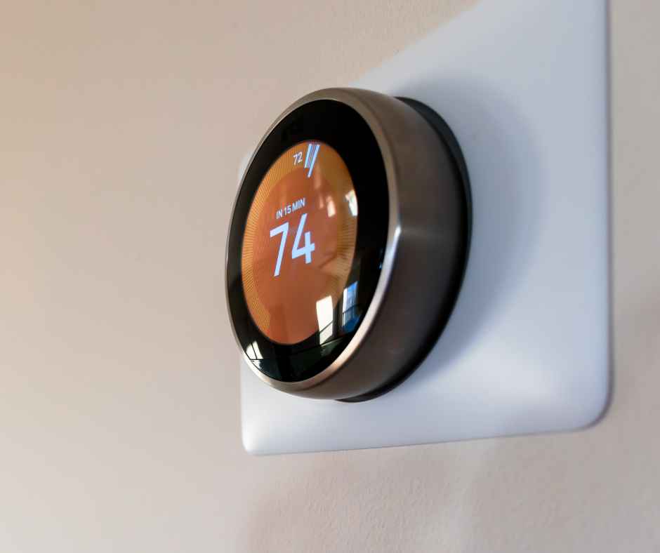 Thermostat on a wall displaying 74 degrees in warm light.