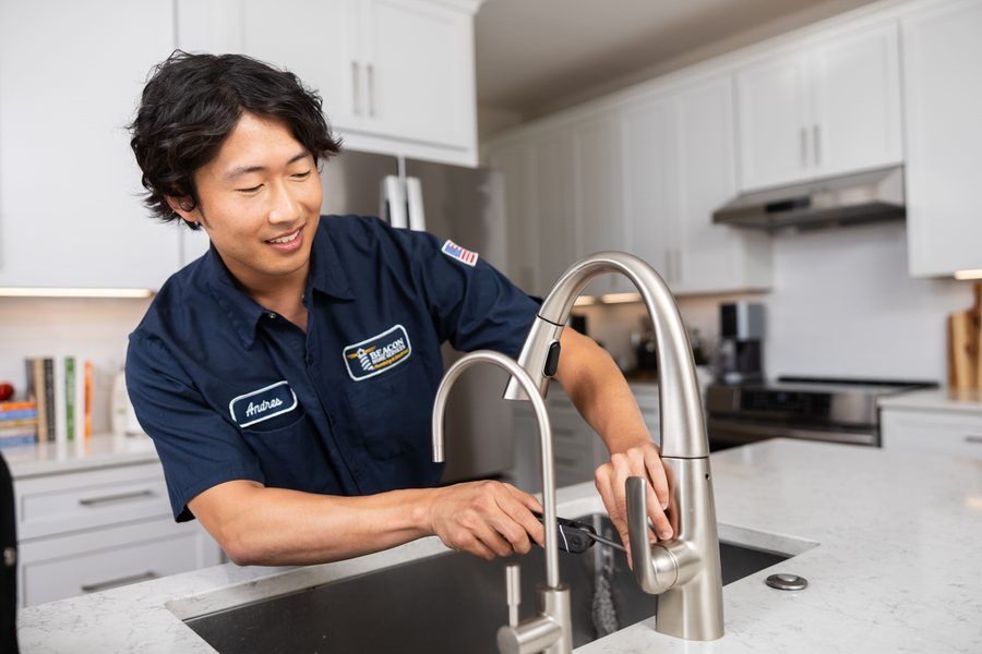 Professional plumber in a navy uniform installs a modern kitchen faucet over a white countertop.