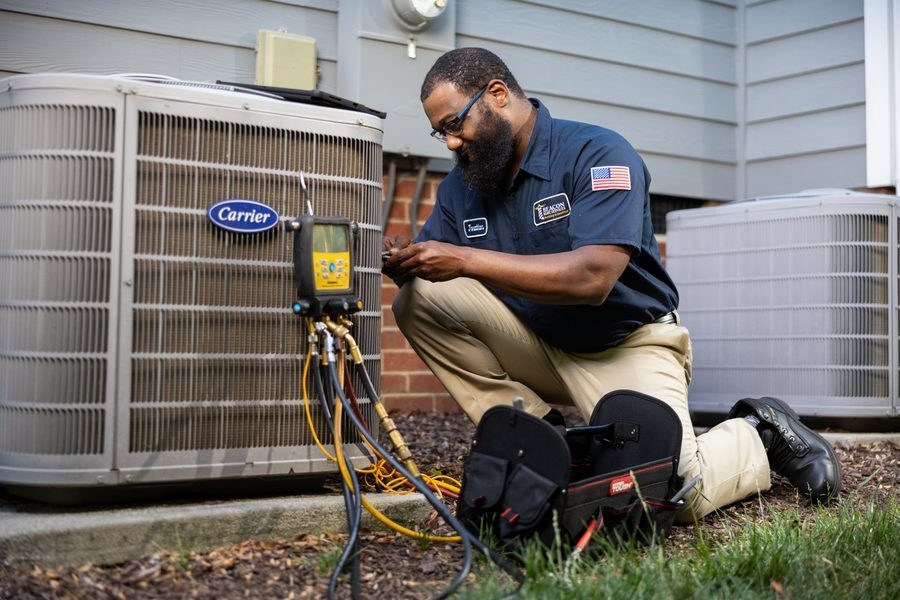 HVAC technician kneeling beside a Carrier outdoor unit, testing with diagnostic gauges and wires.