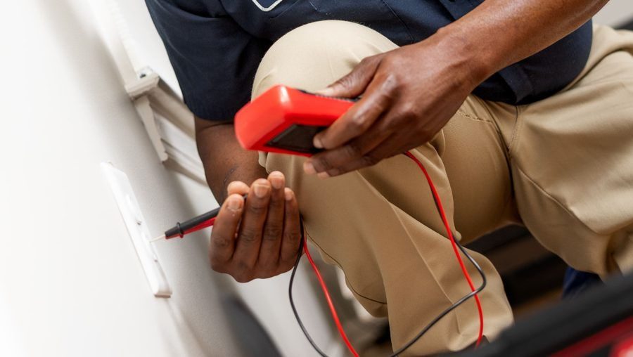 Technician testing an electrical outlet with a red handheld multimeter and probes.