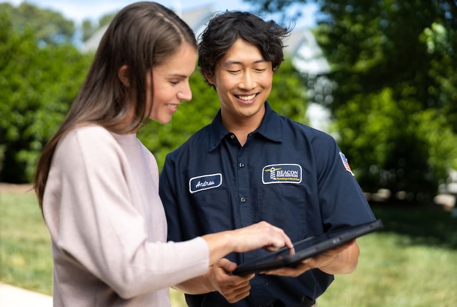 Two people stand in a sunny park, looking at a tablet together; one wears a dark blue work shirt with patches, including 'Beacon' and the name 'Andres'.