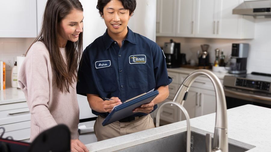 Service technician explains options to a woman in a bright kitchen, holding a clipboard.