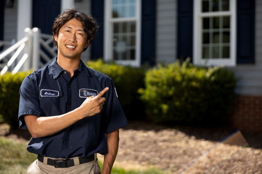 Smiling technician named Andres in a navy uniform points to his company patch on the chest, in front of a suburban house.