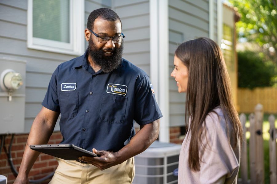 Bearded man in a navy service uniform with a name patch 'Jonathan' shows a tablet to a woman outside a house, explaining something.