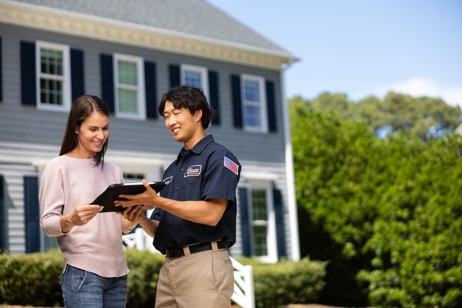 Two people review a tablet outside a suburban home; a home inspector or agent explains details to the client.