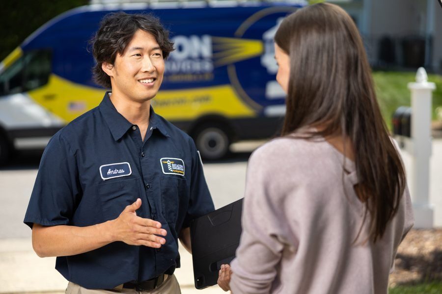 Man in a navy uniform named Andres talks with a woman outdoors, holding a folder, with a blue service van in the background.