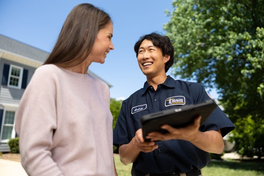 Professional technician in a dark blue uniform showing a tablet to a smiling woman outdoors beside a suburban house.