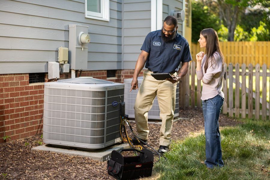 HVAC technician and a woman outside a house reviewing an air conditioning unit with a tablet and toolbox nearby.