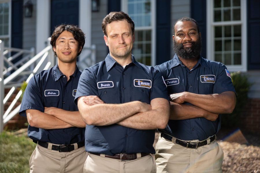 Three uniformed workers with arms crossed posing in front of a suburban house.