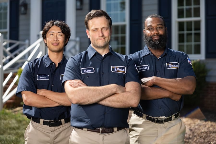 Three uniformed workers stand with arms crossed outside a house, posing for a team photo.