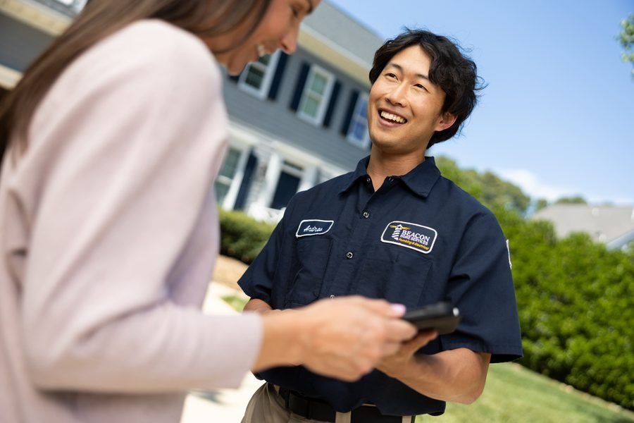 Friendly service technician in a dark blue uniform chats with a customer outside, holding a handheld device.