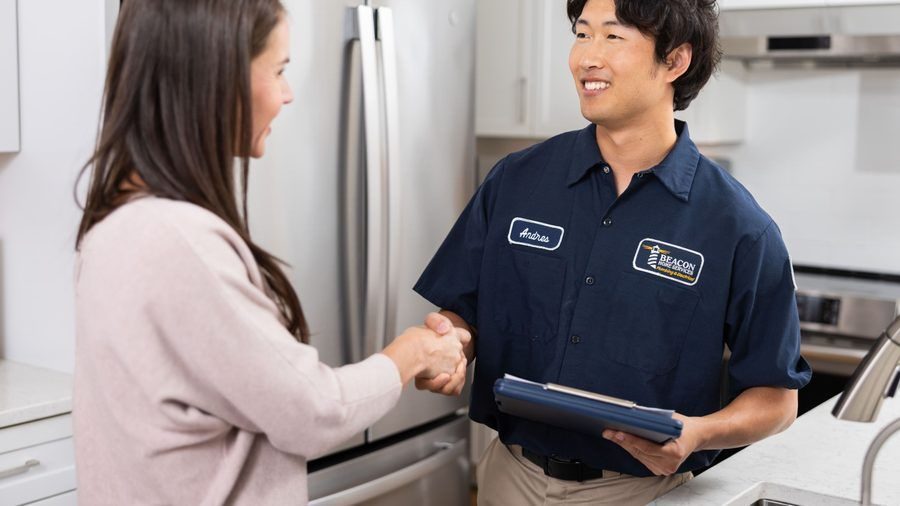 Service technician in a navy shirt shakes hands with a customer in a kitchen, holding a clipboard.