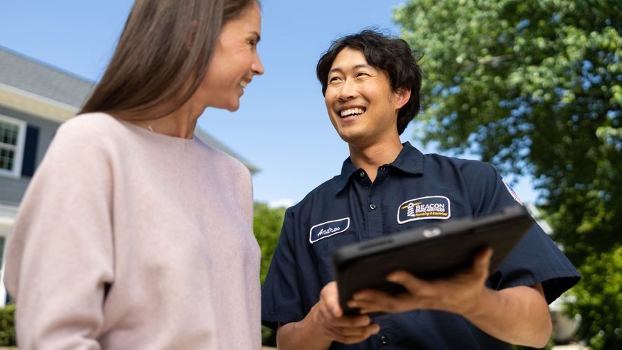 Friendly technician in a navy uniform shows a clipboard to a smiling woman outside a house on a sunny day.